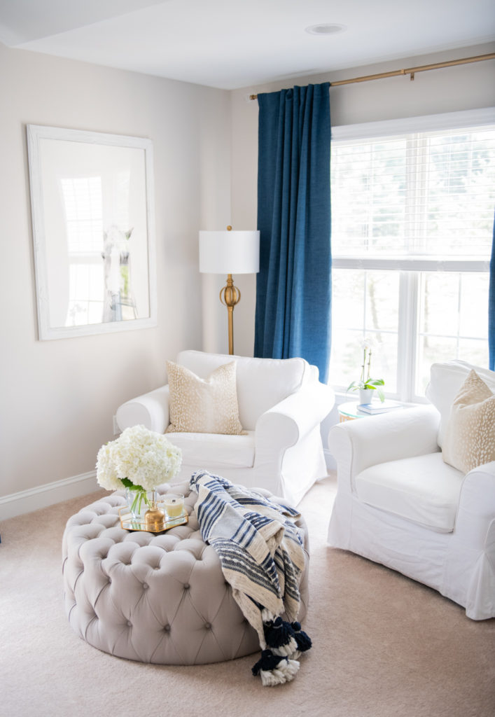 Master Bedroom Remodel Ideas by popular Ohio lifestyle blog, Coffee Beans and Bobby Pins: image of a master bedroom with white armchairs, blue curtains, gold curtain rod, and a grey tufted ottoman. 