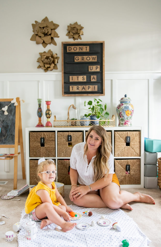 Art Display Ideas by popular Ohio life and style blog, Coffee Beans and Bobby Pins: image of a mom and her young daughter sitting on the floor in their playroom in front of a letterboard and cube storage unit and having a picnic with play food. 