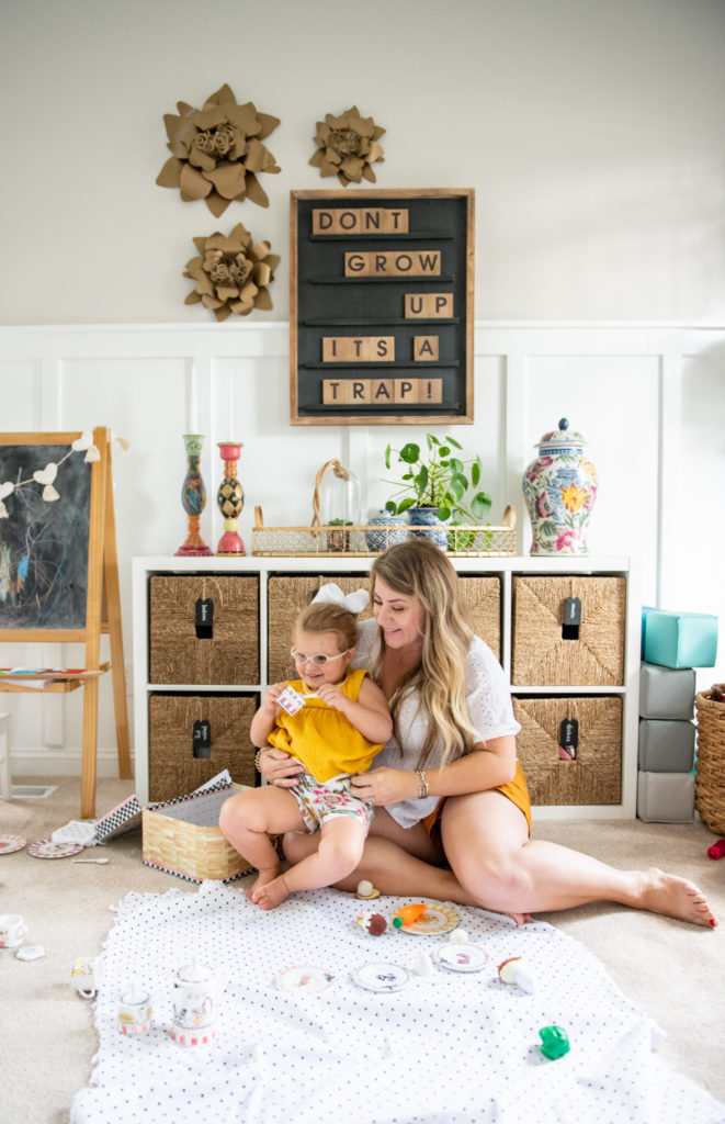 Art Display Ideas by popular Ohio life and style blog, Coffee Beans and Bobby Pins: image of a mom and her young daughter sitting on the floor in their playroom in front of a letterboard and cube storage unit and having a picnic with play food. 