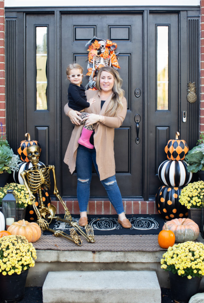 Halloween Front Porch by popular Ohio life and style blog, Coffee Beans and Bobby Pins: image of a mom holding her daughter on their front porch decorated with pumpkins, potted mums, a gold skeleton, Grandin Road Pumpkin decor. 