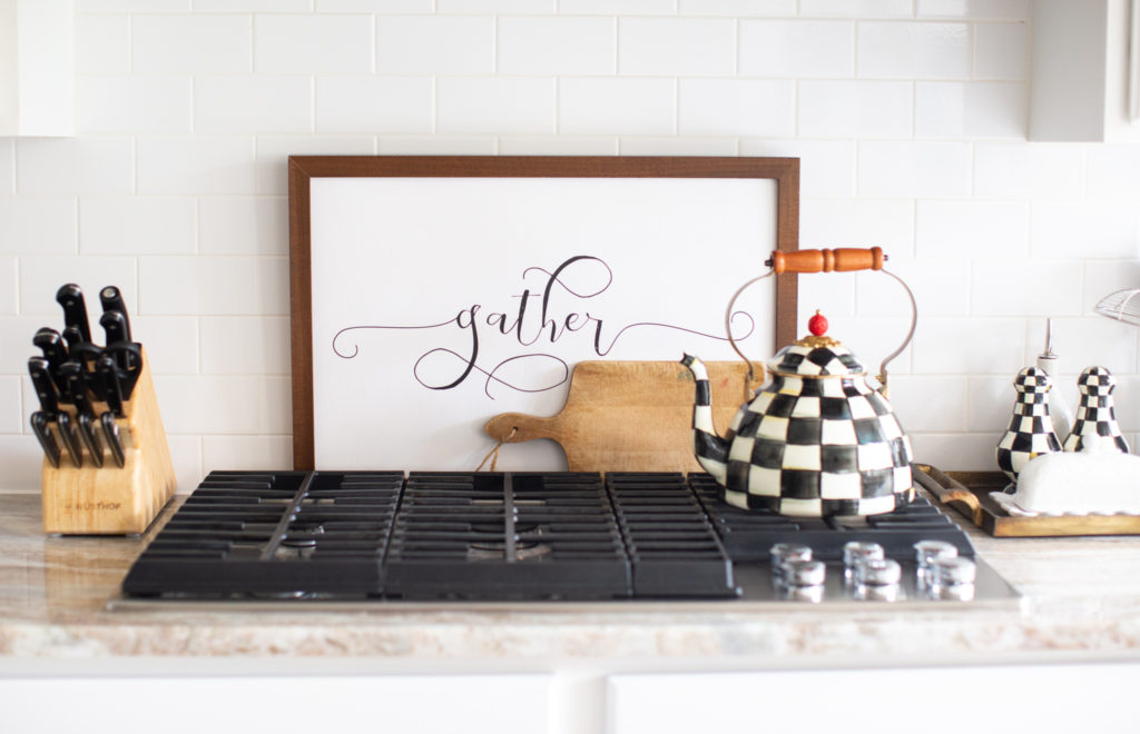 Home Tour by popular Ohio lifestyle blog, Coffee Beans and Bobby Pins: image of a gas range stove, Mackenzie Childs tea pot, Mackenzie Childs salt and pepper shakers, gather sign, and wooden cutting board. 