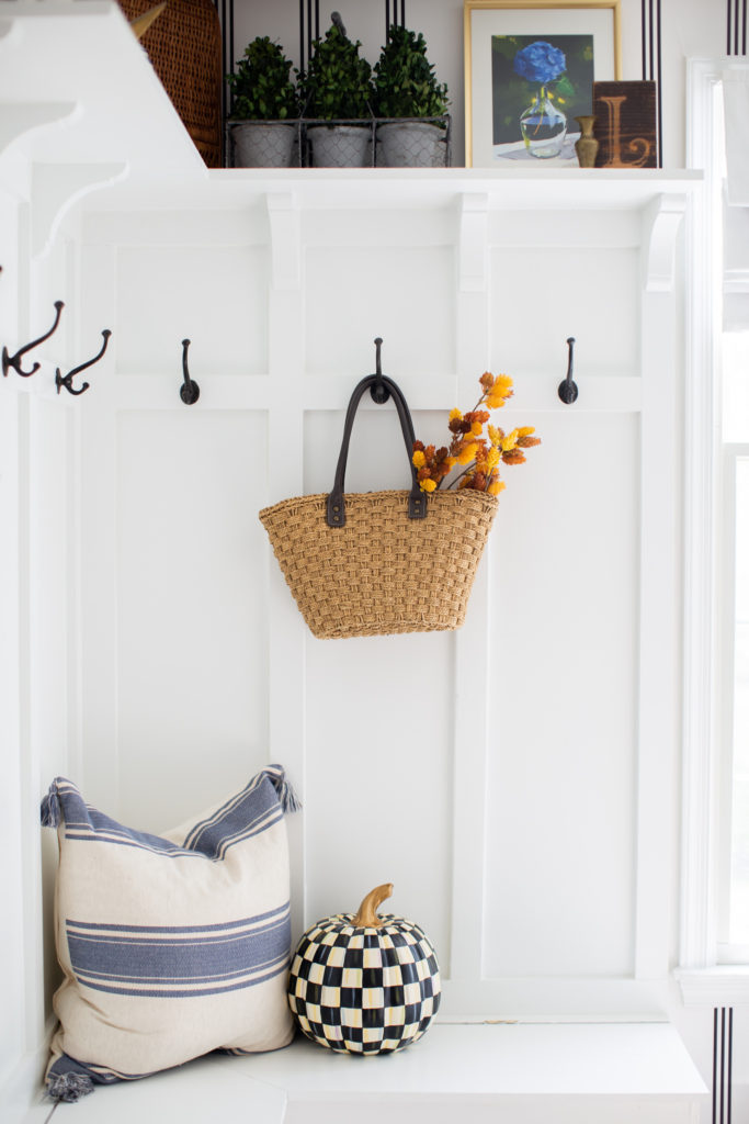 Home Tour by popular Ohio lifestyle blog, Coffee Beans and Bobby Pins: image of a mudroom bench decorated with a blue and white stripe tassel pillow and Mackenzie Childs Courtly Check pumpkin. 