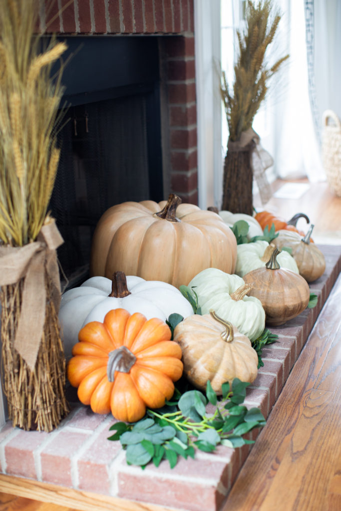 Home Tour by popular Ohio lifestyle blog, Coffee Beans and Bobby Pins: image of  faux pumpkins and faux eucalyptus branches on a fireplace bench. 