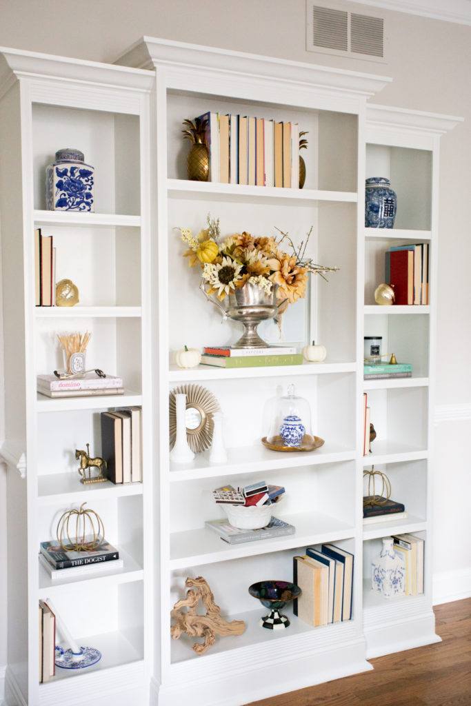 Home Tour by popular Ohio lifestyle blog, Coffee Beans and Bobby Pins: image of a white bookcase decorated with books, blue and white china, faux floral arrangement, and gold fall decor. 