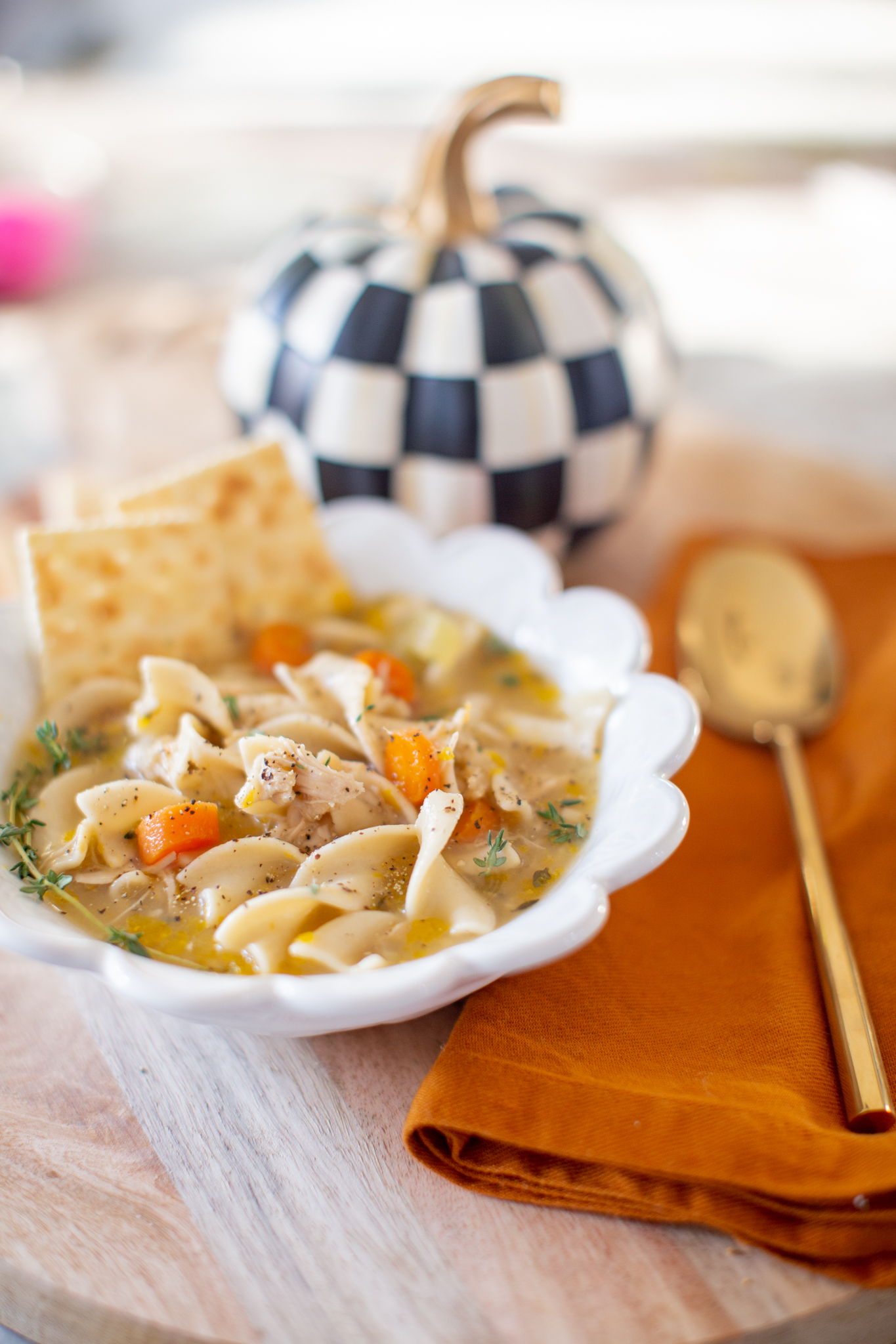 Homemade Chicken Noodle Soup by popular Ohio lifestyle blog, Coffee Beans and Bobby Pins: image of homemade chicken noodle soup in a white scallop edge bowl next to an orange cloth napkin, gold spoon, and pile of soda crackers. 