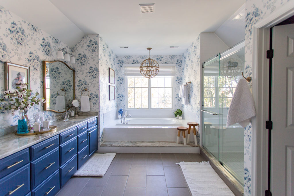 Master Bedroom Remodel by popular Ohio life and style blog, Coffee Beans and Bobby Pins: image of master bathroom with blue and white floral wallpaper, gold light fixture, white rugs, blue vanity and gold frame mirrors. 