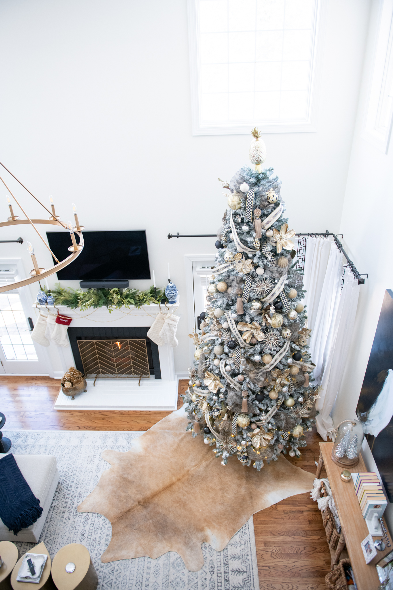 Christmas Home Decor Ideas by popular Ohio life and style blog, Coffee Beans and Bobby Pins: image of a living room decorated with a 12 foot flocked Christmas tree decorated with Mackenzie-Childs ornaments, pearl garland, and cream knit stockings. 