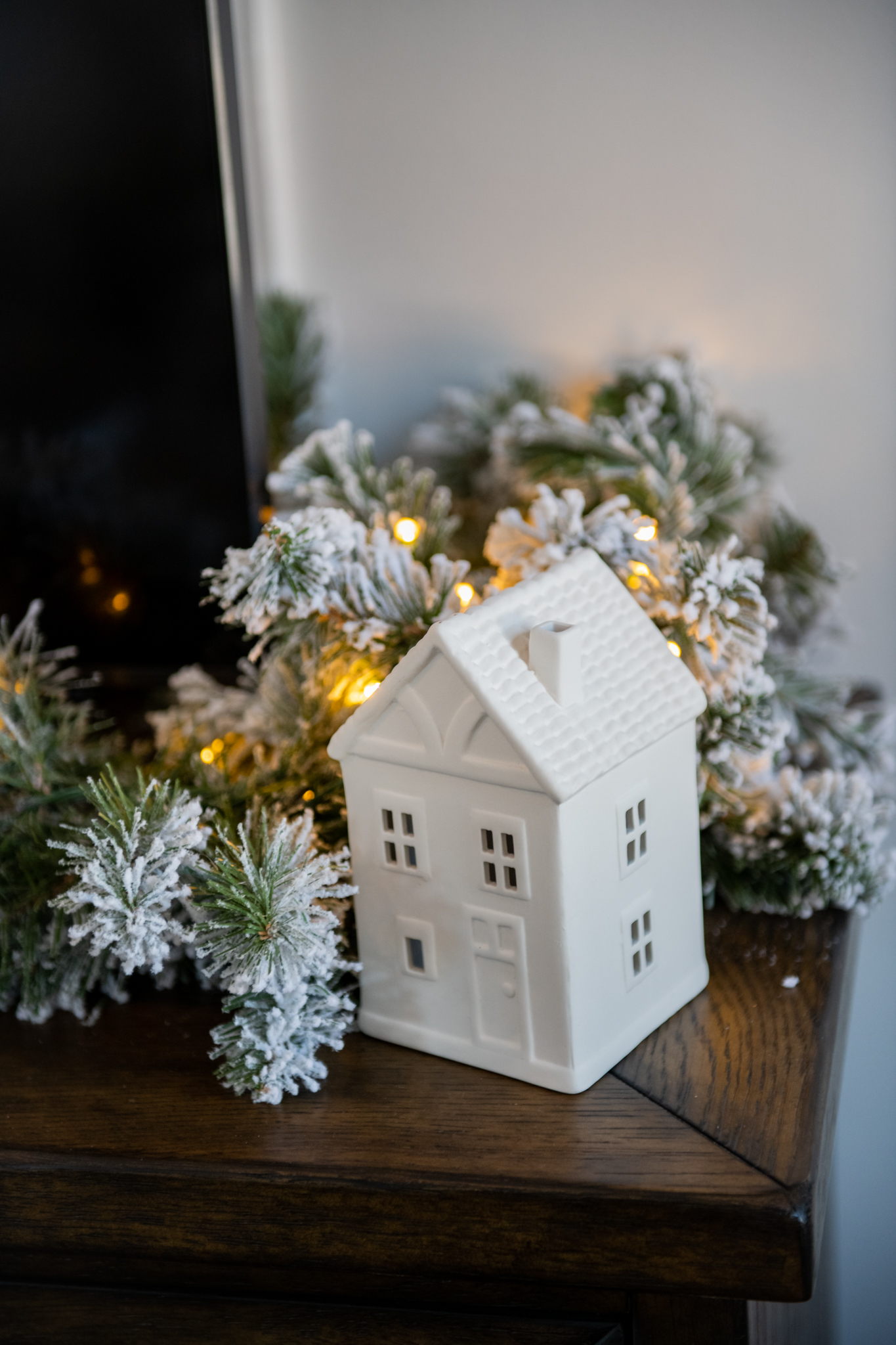 Christmas Home Tour by popular Ohio life and style blog, Coffee Beans and Bobby Pins: image of a white ceramic house next to a flocked garland. 