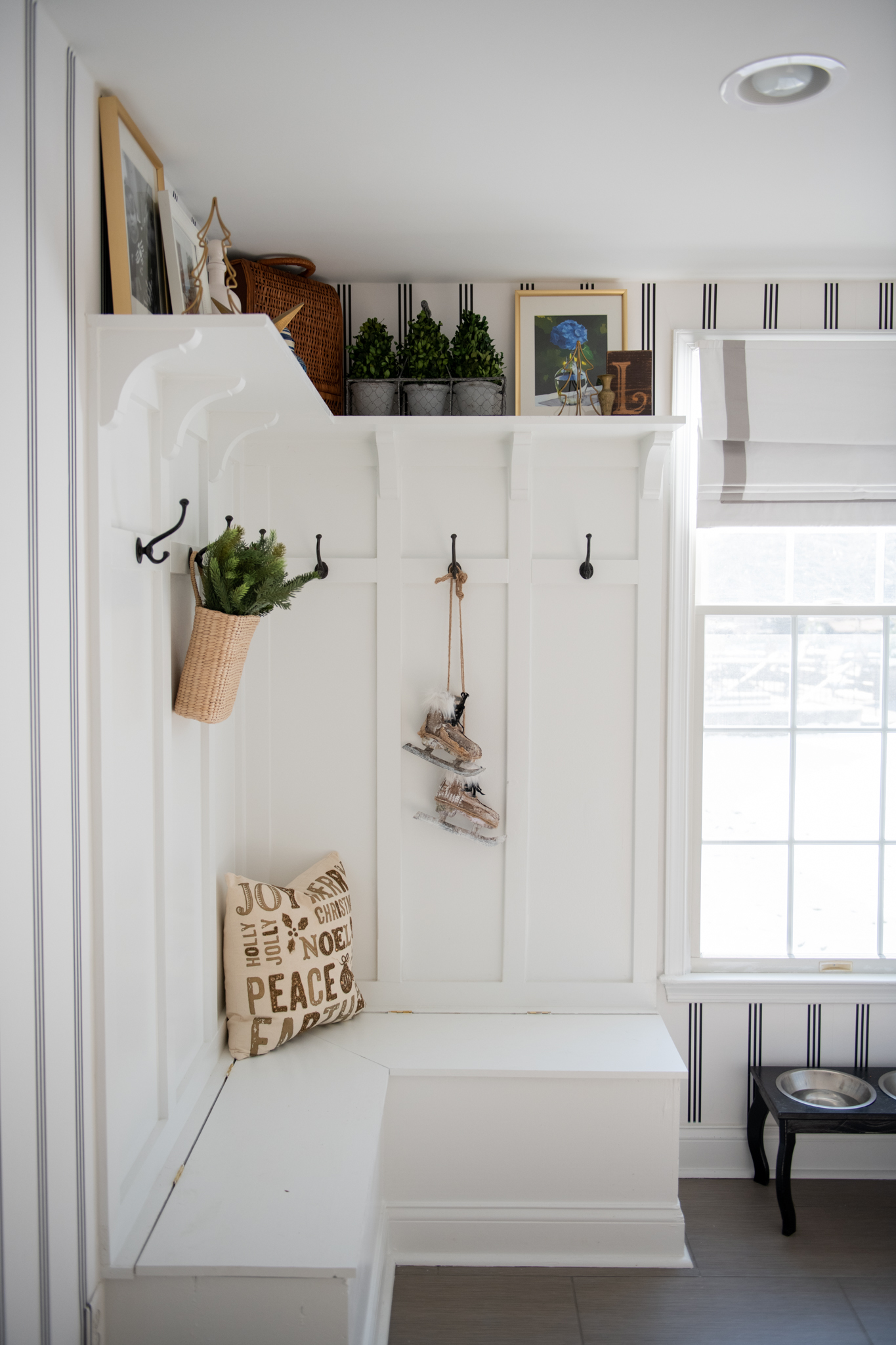 Christmas Home Decor Ideas by popular Ohio life and style blog, Coffee Beans and Bobby Pins: image of a mudroom decorated with ice skates decor, Christmas throw pillow basket filled with pine tree branches, and mini Christmas tree decor. 