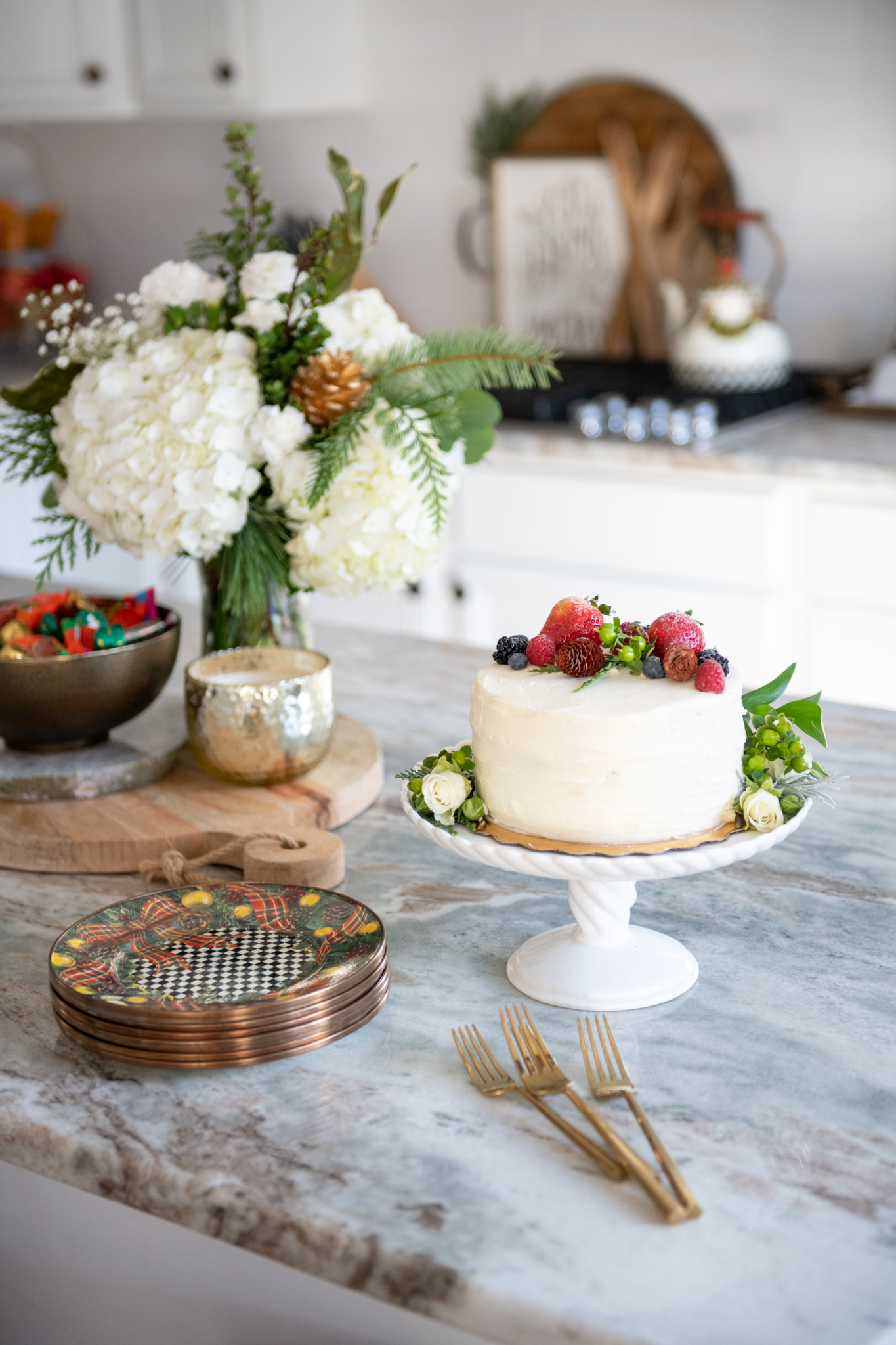 Christmas Home Decor Ideas by popular Ohio life and style blog, Coffee Beans and Bobby Pins: image of a kitchen island that's set with a winter floral arrangement, cake with a winter cake topper, Christmas plates, gold forks, and a gold candle. 