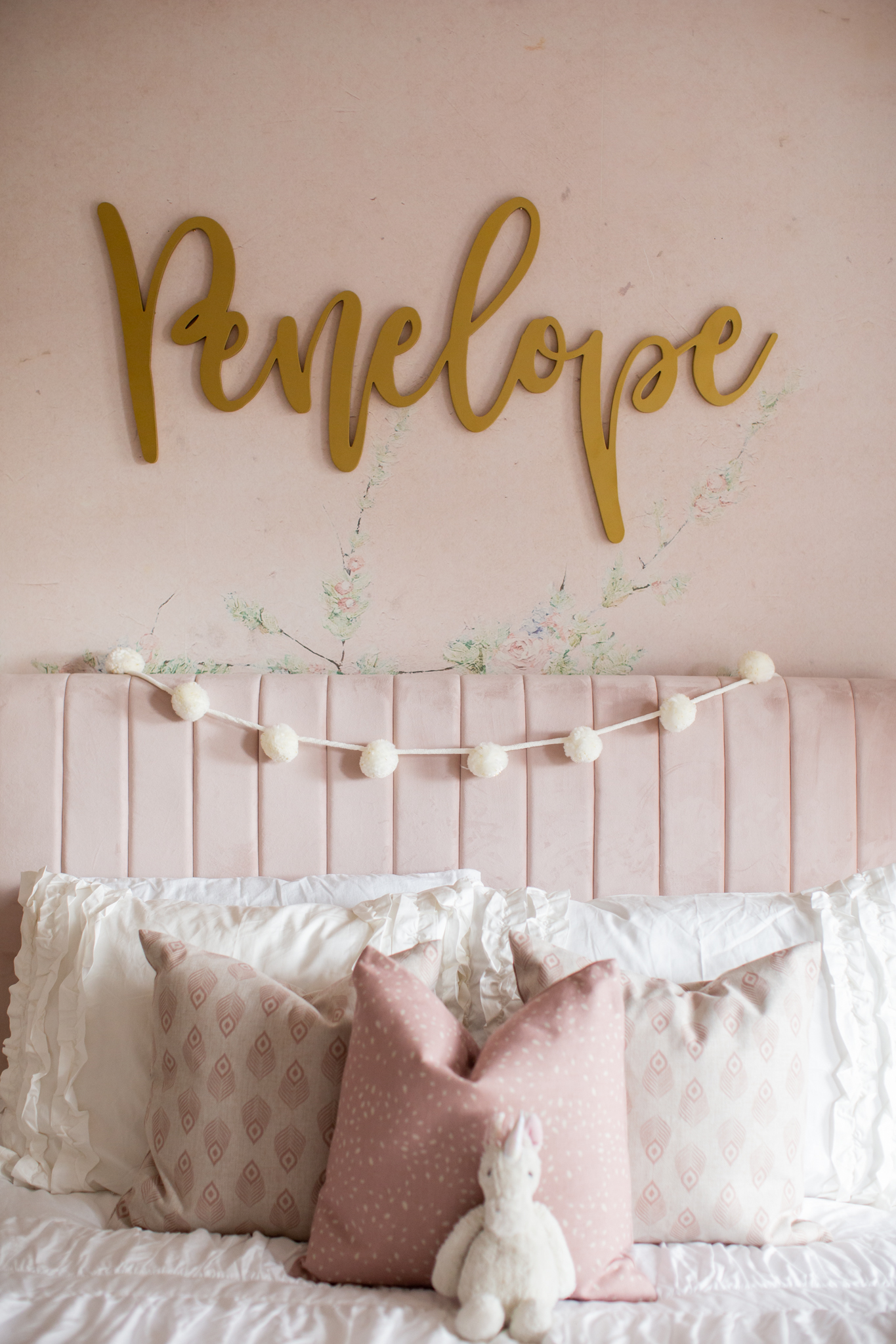 Holiday Decor by popular Ohio life and style blog, Coffee Beans and Bobby Pins: image of a little girls bedroom decorated with pink floral wallpaper, gold name sign, pink headboard, pink bedding, and white pom garland. 