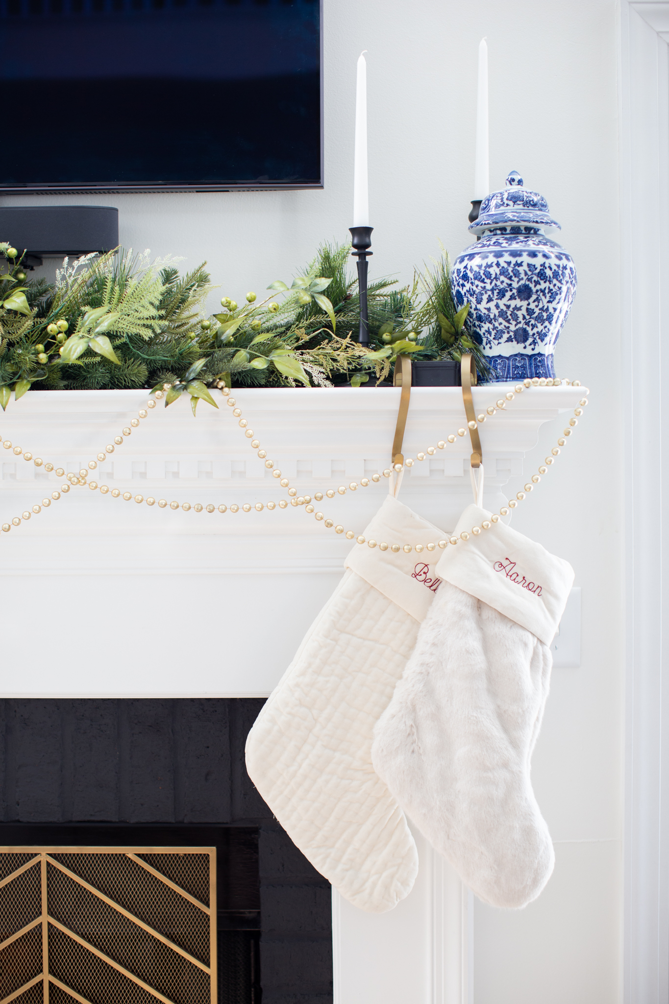 Christmas Home Decor Ideas by popular Ohio life and style blog, Coffee Beans and Bobby Pins: image of a fireplace mantle that's decorated with pearl garland and a cream quilted stocking and white fur stocking. 