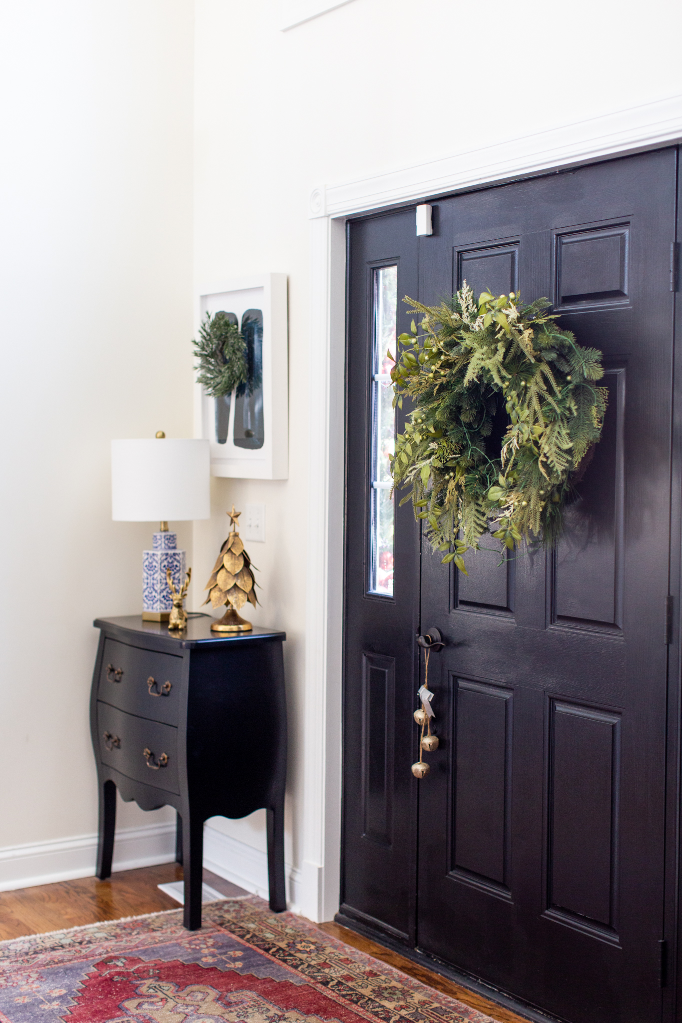 Christmas Home Decor Ideas by popular Ohio life and style blog, Coffee Beans and Bobby Pins: image of a front door decorated with a Christmas wreath and sleigh bells and a side table decorated with a gold pine tree and gold reindeer. 