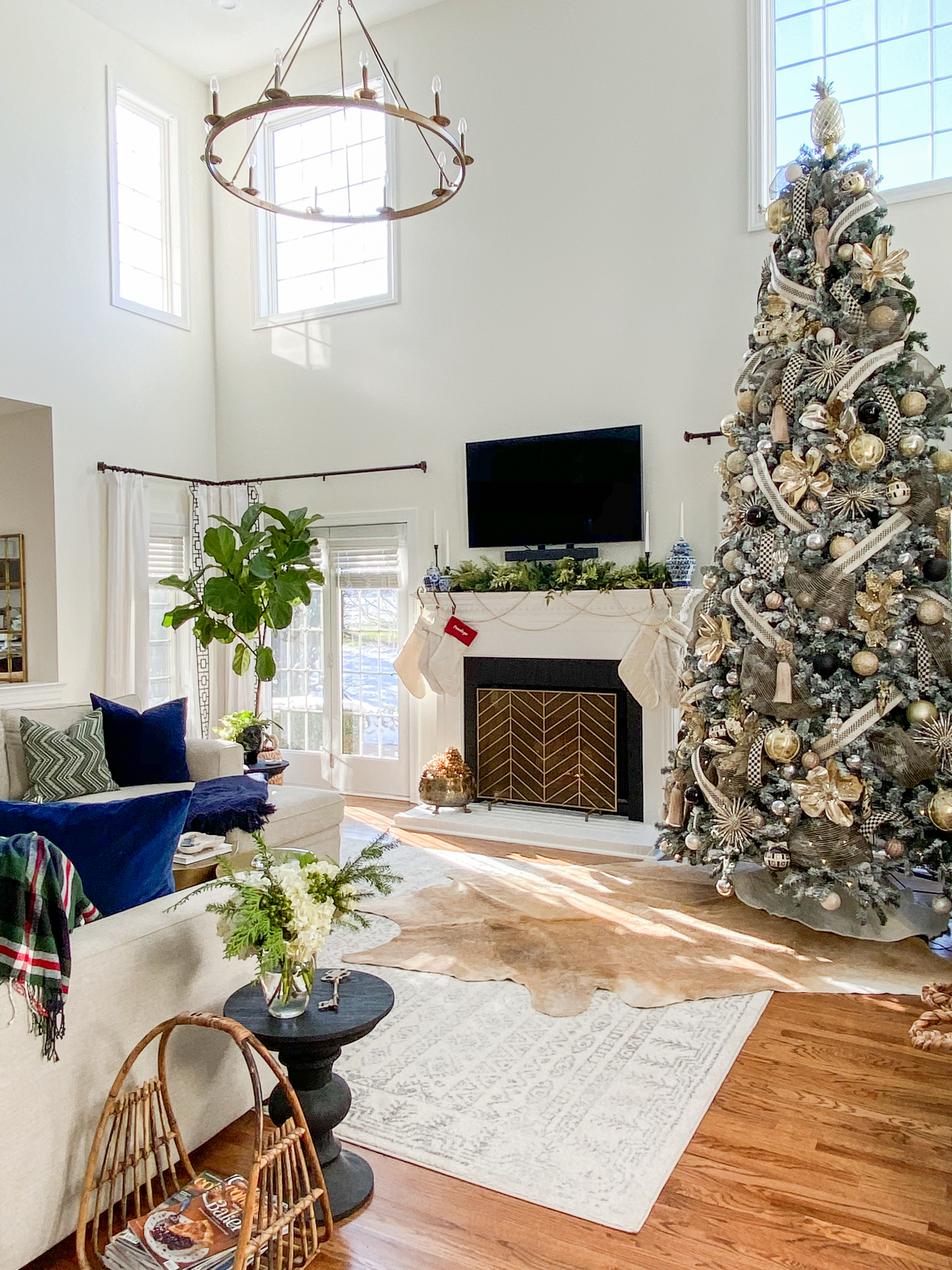 Christmas Home Decor Ideas by popular Ohio life and style blog, Coffee Beans and Bobby Pins: image of a living room decorated with a 12 foot flocked Christmas tree decorated with Mackenzie-Childs ornaments, pearl garland, and cream knit stockings. 