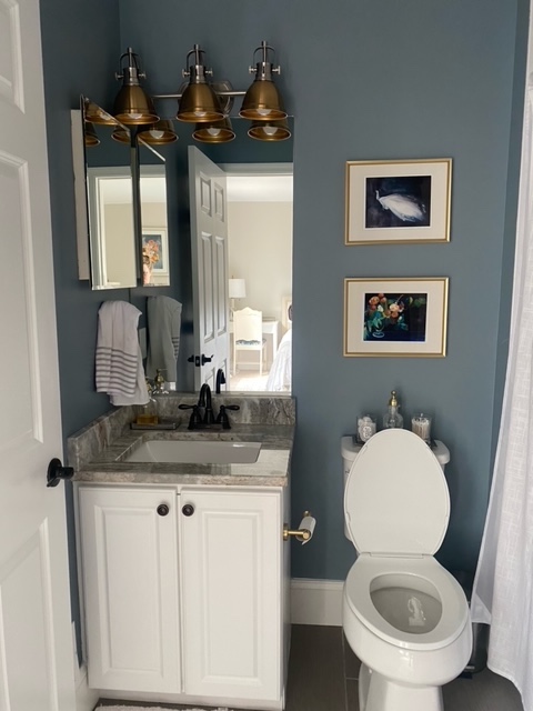 Guest Bathroom Makeover by popular Ohio life and style blog, Coffee Beans and Bobby Pins: image of a guest bathroom with a white vanity, gold towel bar and gold toilet paper dispenser, gold and silver light figure, blue painted walls, and gold framed art. 