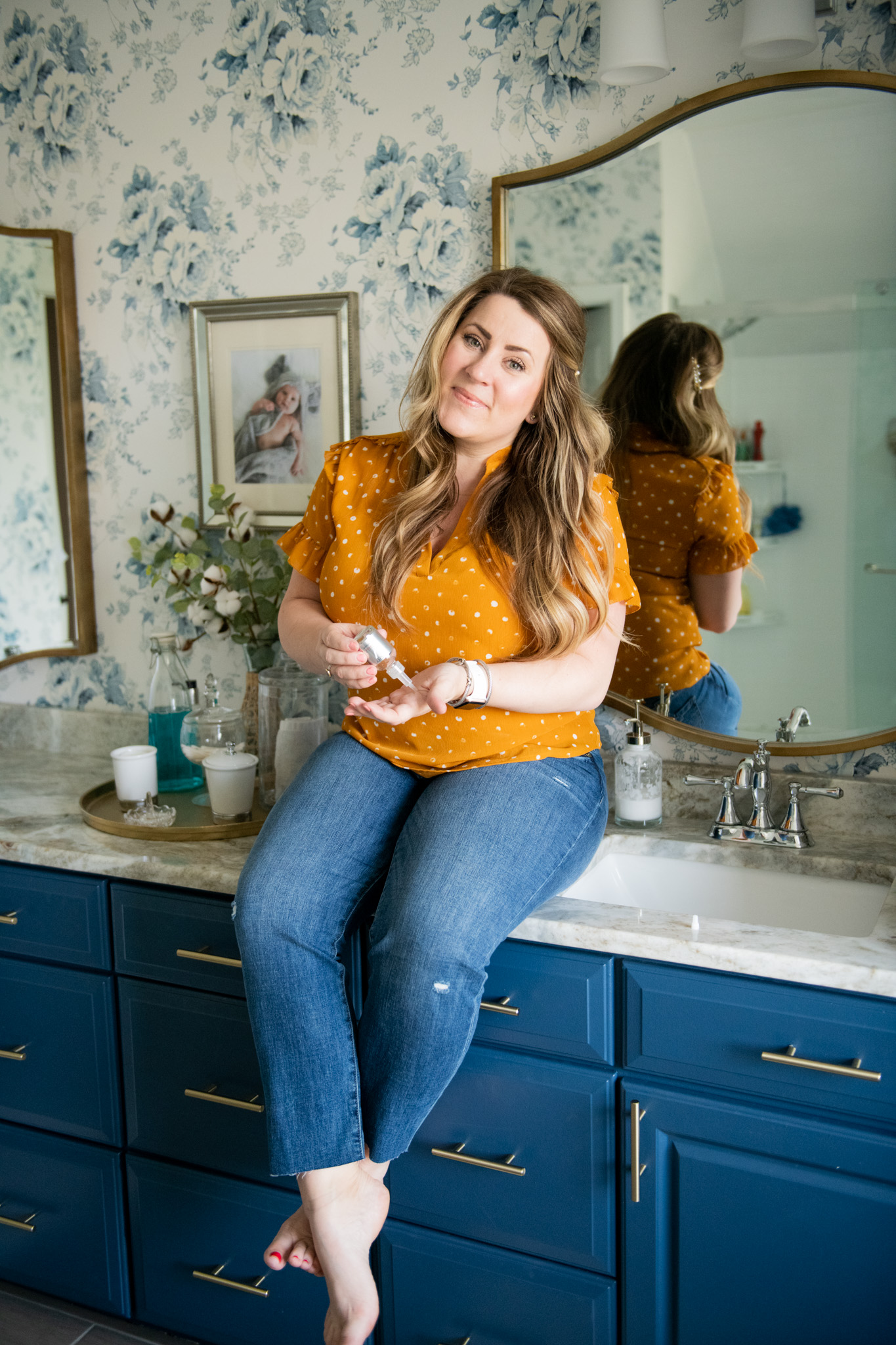 Springtime Products by popular Ohio life and style blog, Coffee Beans and Bobby Pins: image of a woman wearing a orange and white polka dot ruffle sleeve blouse and jeans and sitting on her bathroom vanity