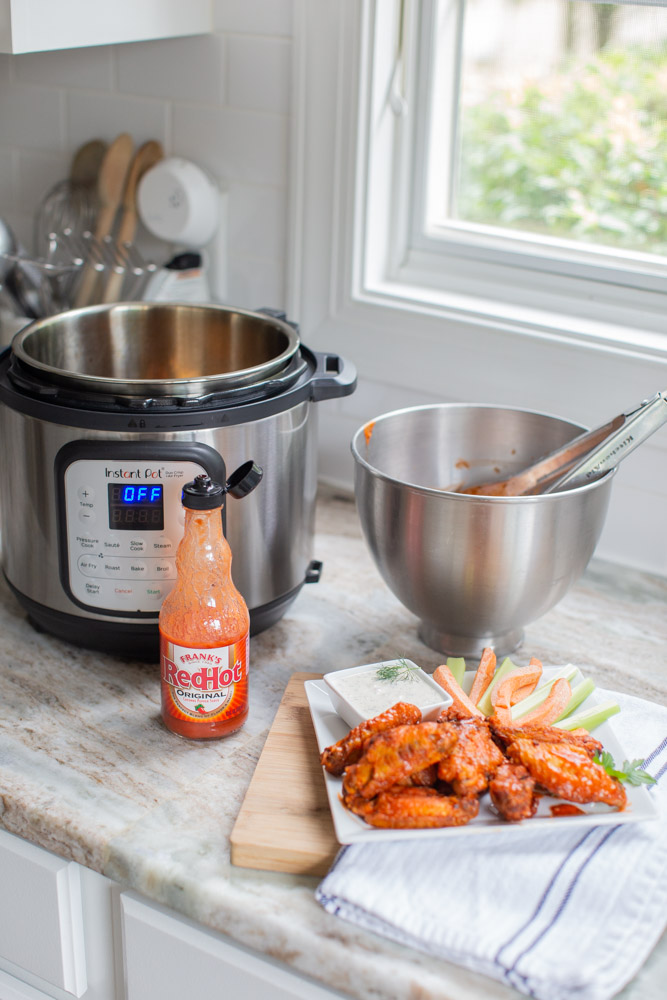 Air Fried Chicken Wings by popular Ohio lifestyle blog, Coffee Beans and Bobby Pins: image of a plate of air fried chicken wings next to a bottle of Frank's hot sauce and a Insta Pot. 